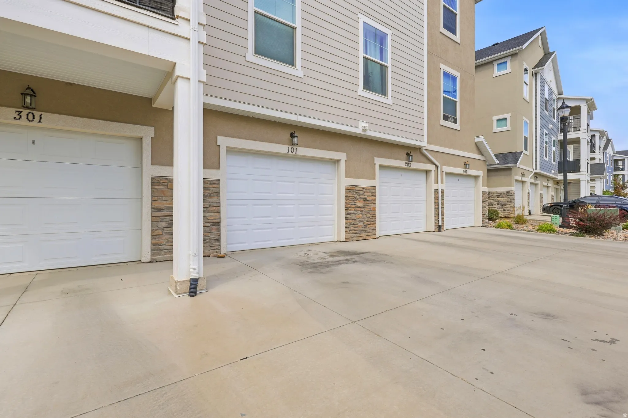 Attached garages with white panel doors, complemented by stone facade accents and tan stucco