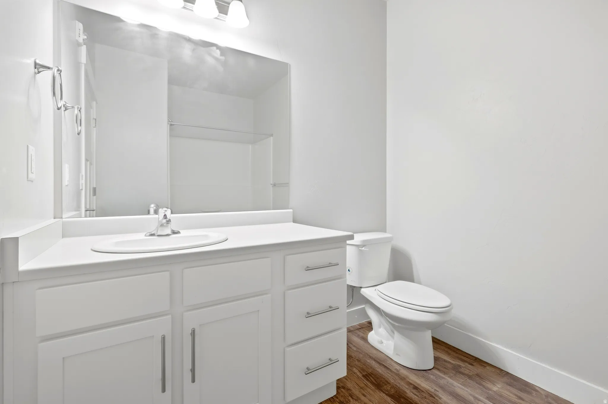 White vanity with integrated sink, chrome faucet, white countertop, and wood-finish flooring