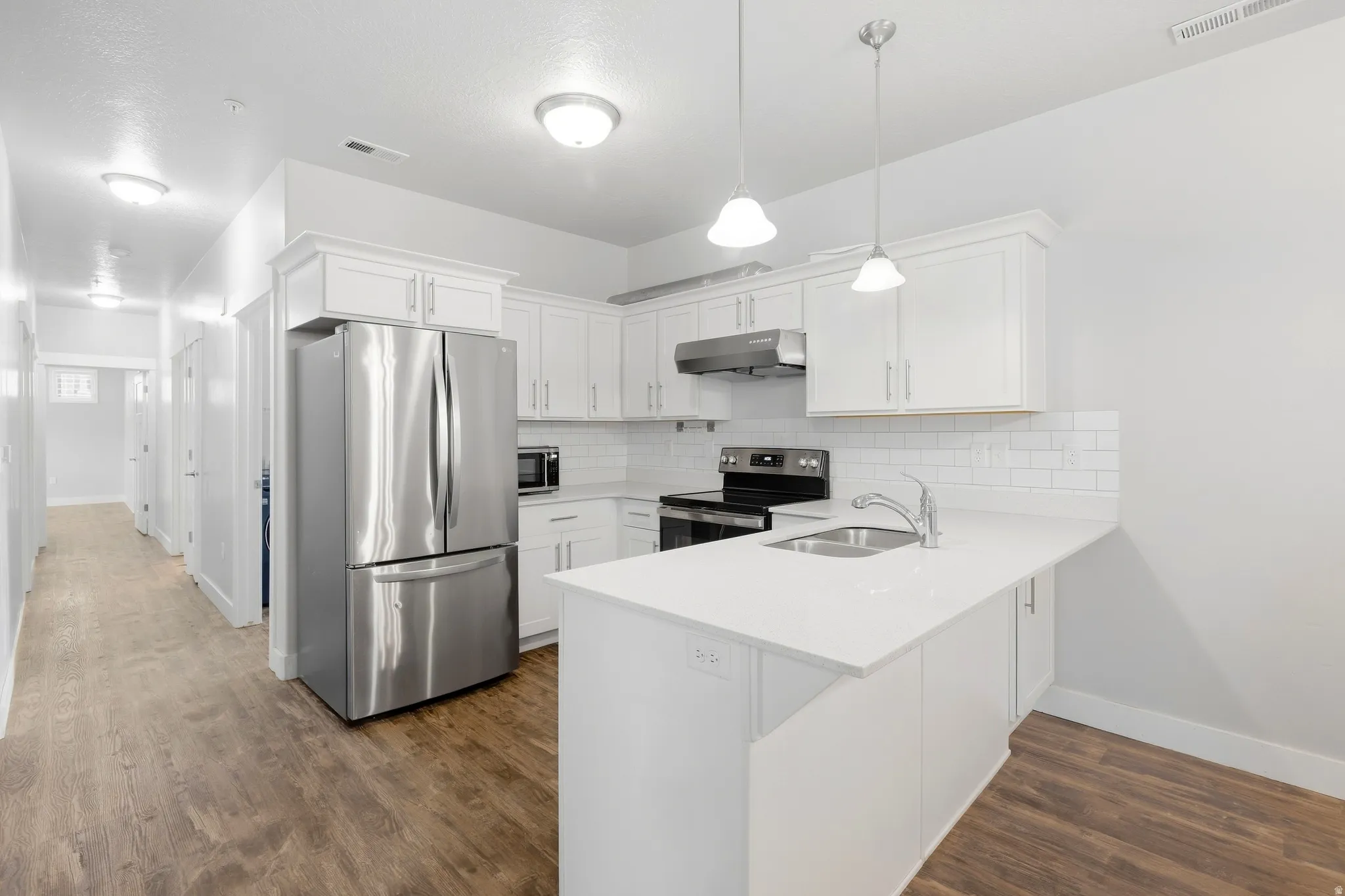 Kitchen featuring white cabinetry, stainless steel appliances, a white subway tile backsplash, a countertop island, and wood-finish flooring