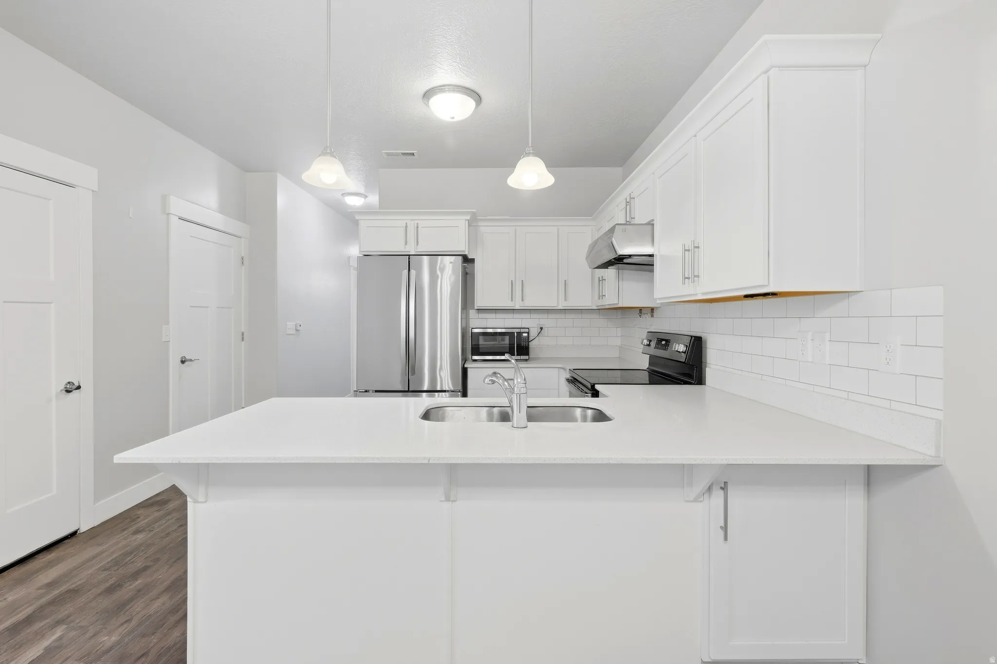 Kitchen featuring white cabinetry, stainless steel appliances, white subway tile backsplash, a peninsula with a stainless steel sink, and wood-finish flooring