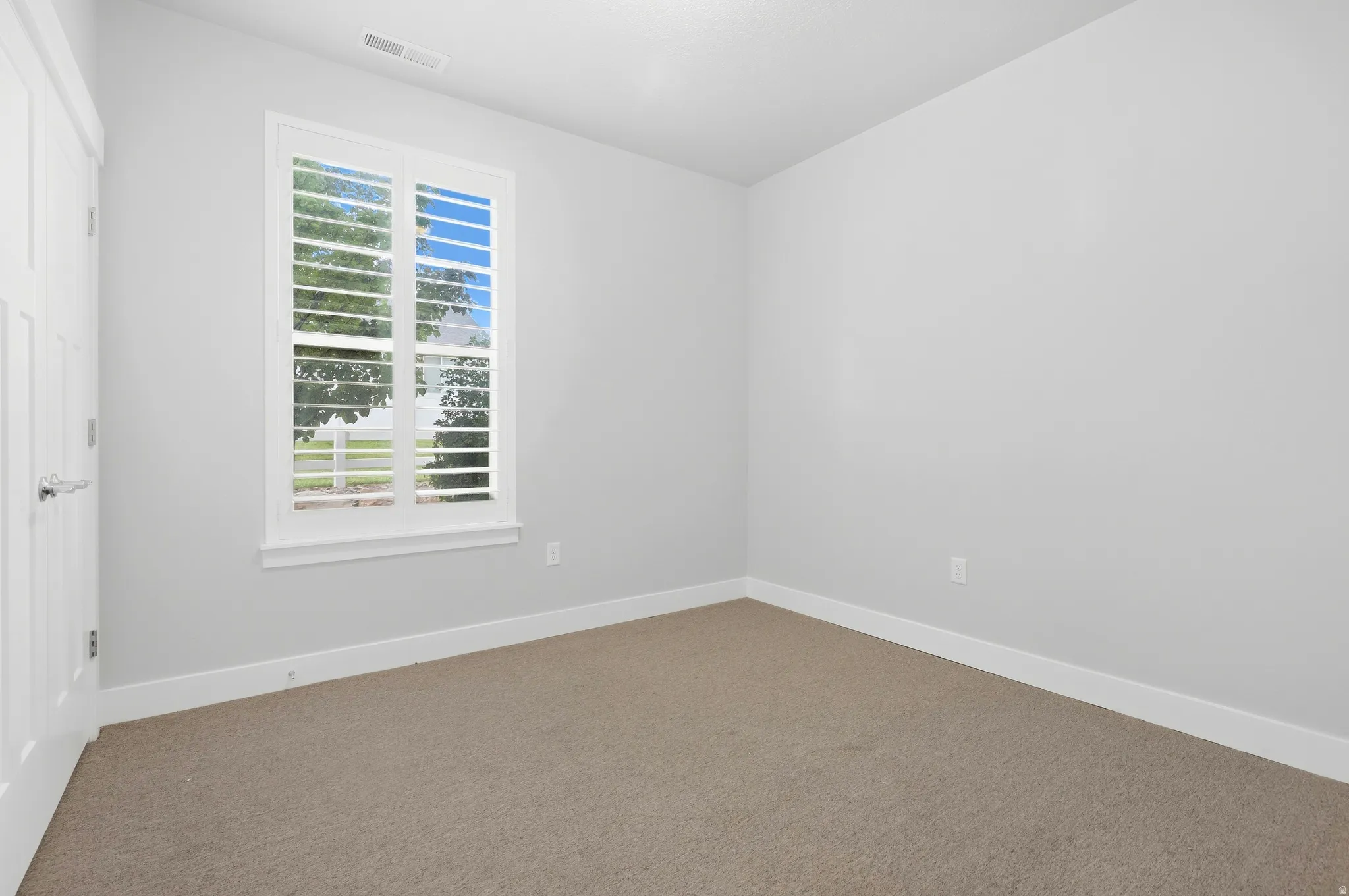 Window with white plantation shutters, light gray wall finish, and neutral carpet flooring