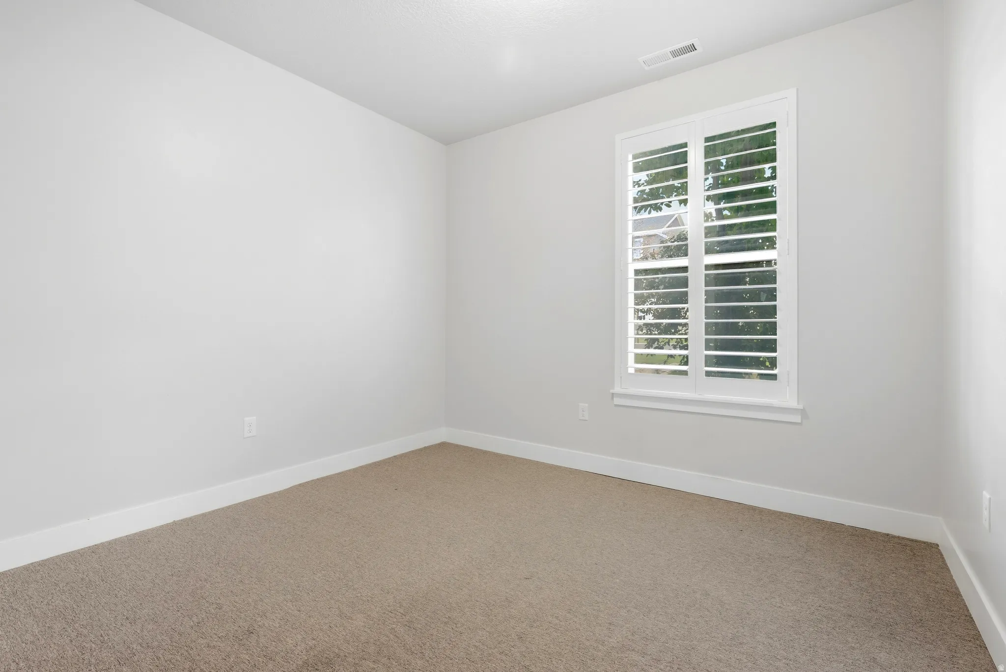 Recessed window with white plantation shutters, carpeted flooring, and light-colored wall finishes