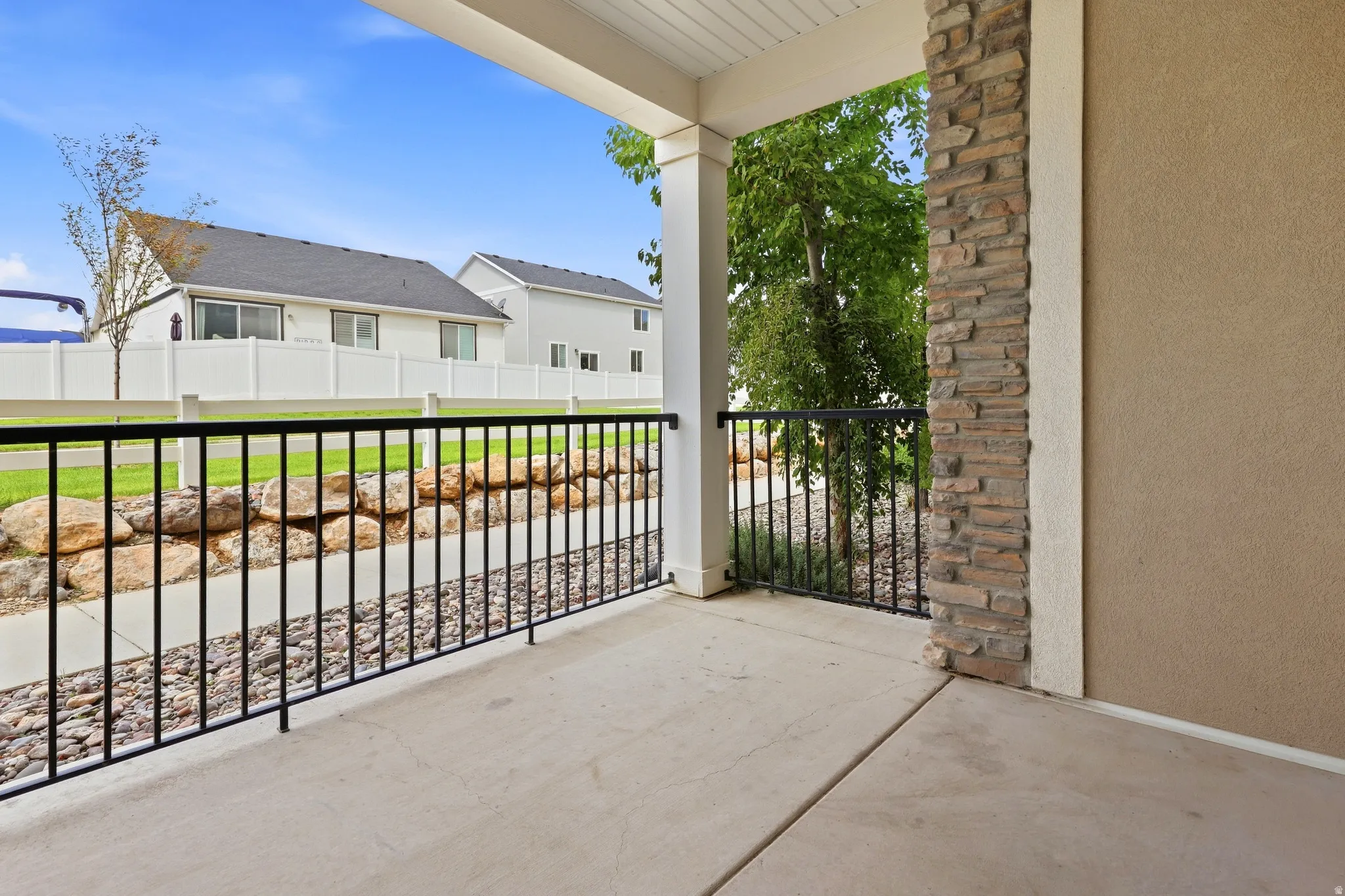 Covered patio featuring concrete flooring, black metal railing, and a stacked stone pillar accent