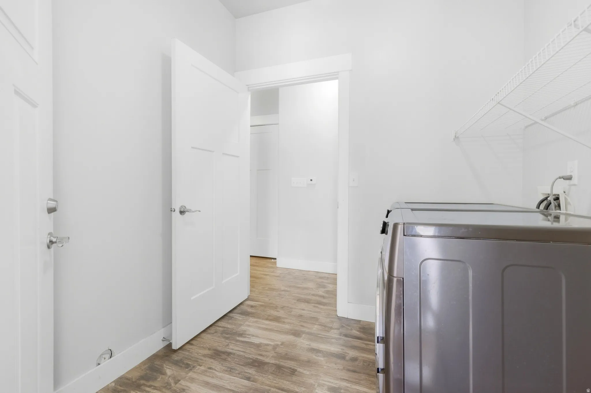 Laundry area with wood-finish flooring, white walls, and built-in wire shelving
