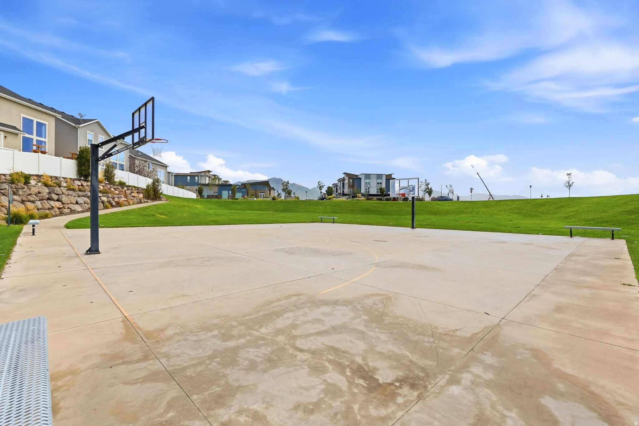Concrete basketball court featuring two hoops, adjacent to a manicured grassy area
