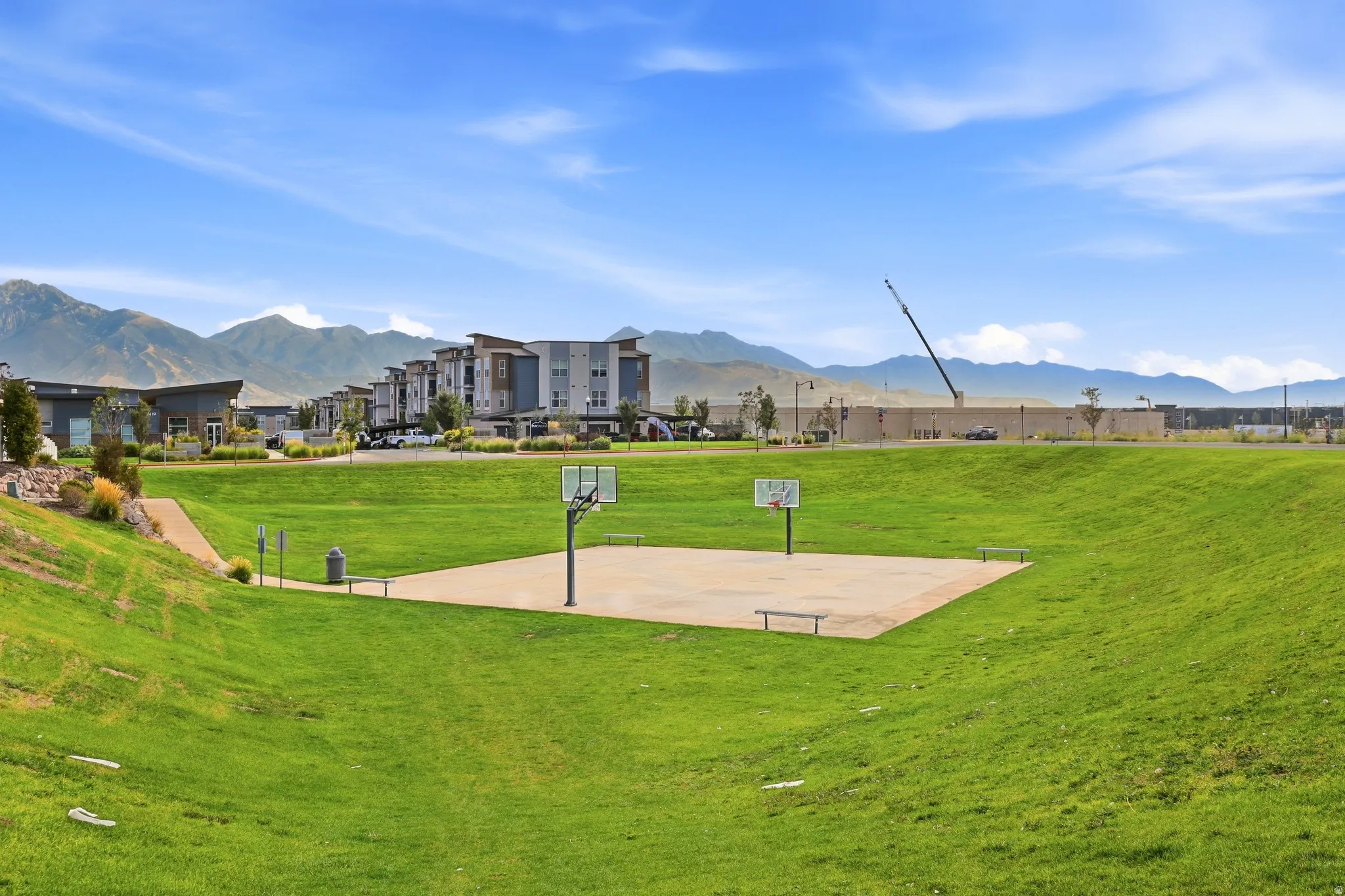 Expansive green space featuring a concrete sports court with two basketball hoops and surrounding benches
