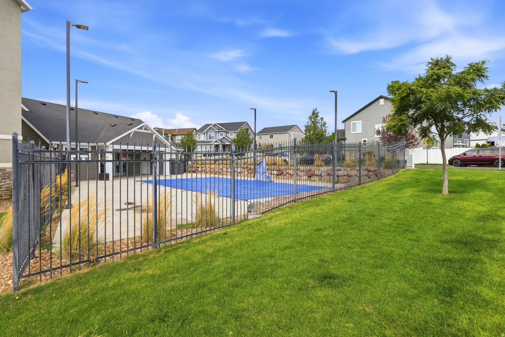 Fenced exterior leisure area with a covered pool and surrounding patio, featuring mature landscaping and a grassy expanse