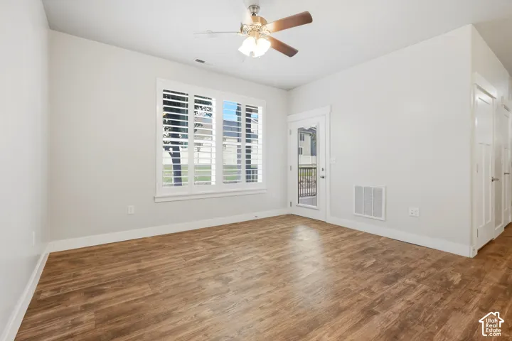 Wood-finish flooring, ceiling fan with integrated lighting, white plantation shutters, glass-paneled exterior door, and white interior doors