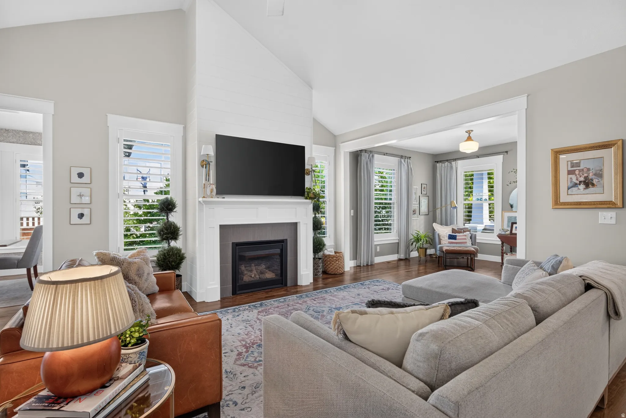 Vaulted ceiling with shiplap accent wall, built-in fireplace with white mantel, plantation shutters, and wood-finish flooring