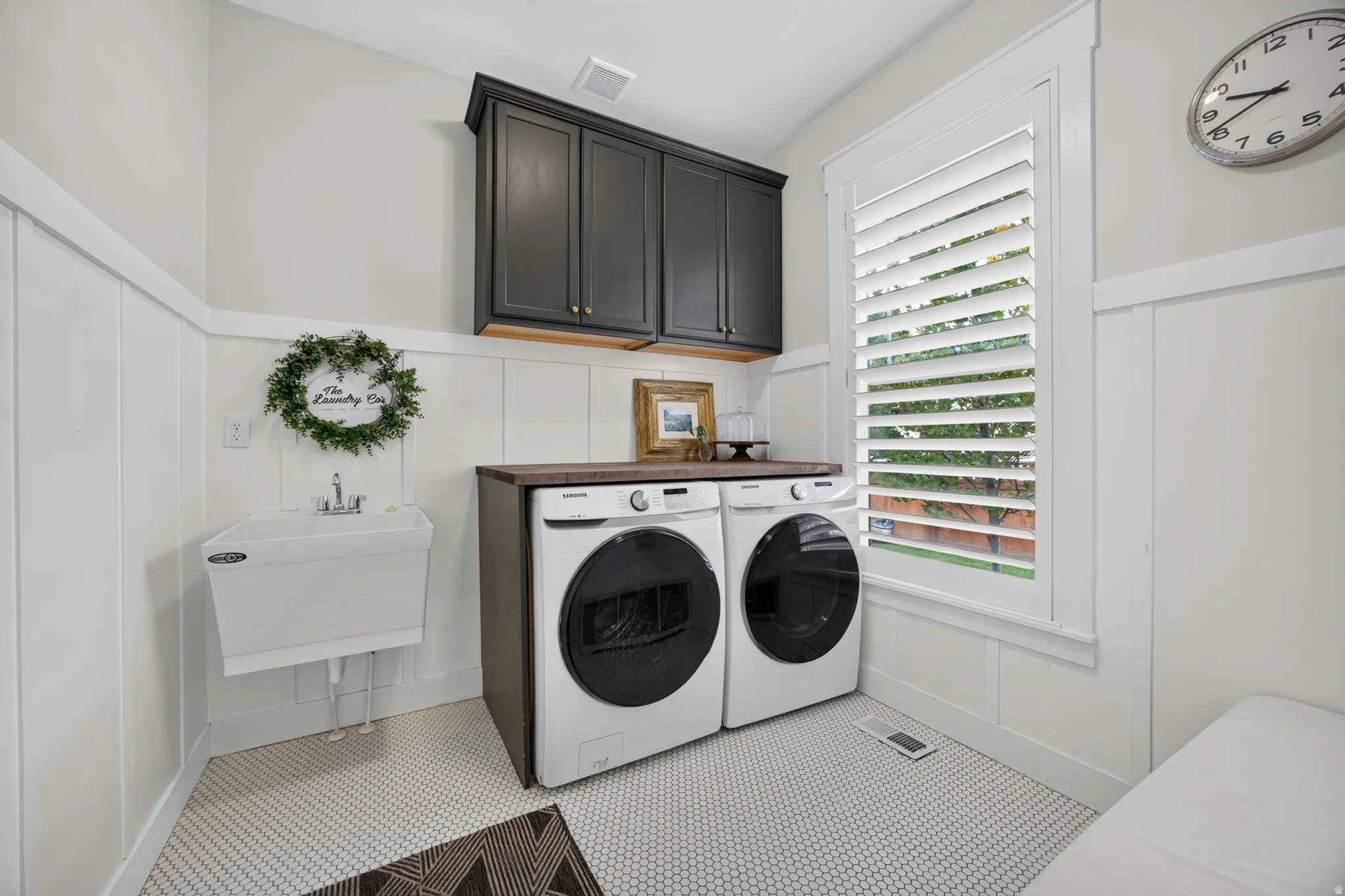 White board and batten wall paneling, white hexagonal tile flooring, built-in dark cabinetry, and a utility sink