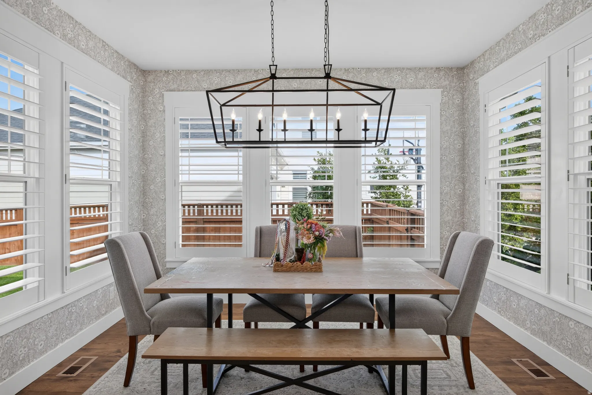 Hardwood-style flooring, white window shutters, patterned wall covering, and a contemporary linear chandelier