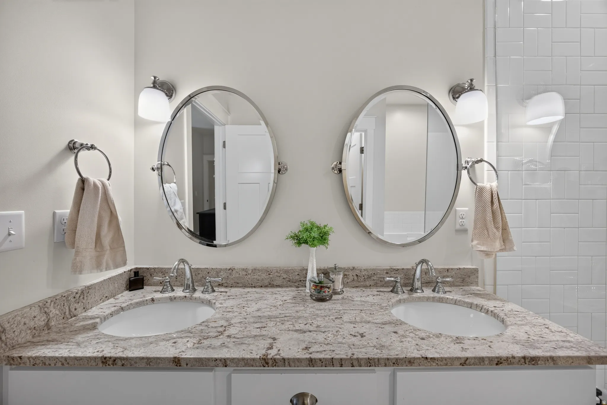 Double vanity with integrated oval sinks, stone-finish countertop, dual oval mirrors, and wall-mounted lighting fixtures