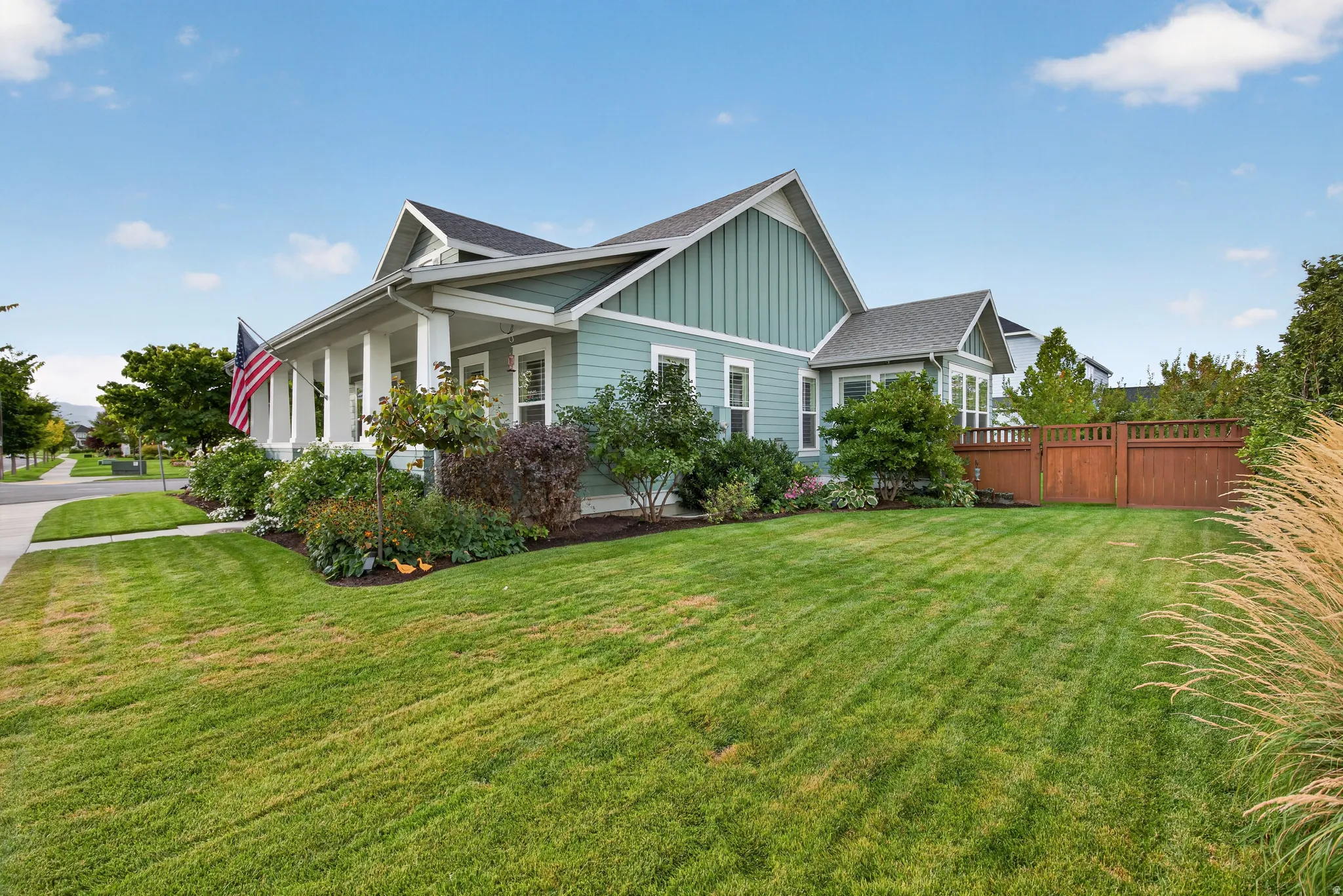 Exterior featuring board and batten siding, a covered porch with white columns, a gabled roofline, mature landscaping, and a wood privacy fence