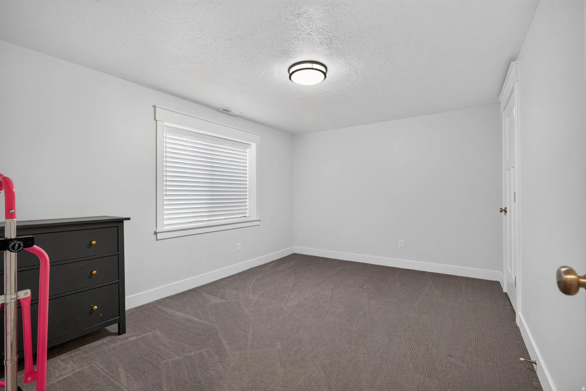 Neutral gray walls with white trim, recessed window with horizontal blinds, and dark gray carpeting