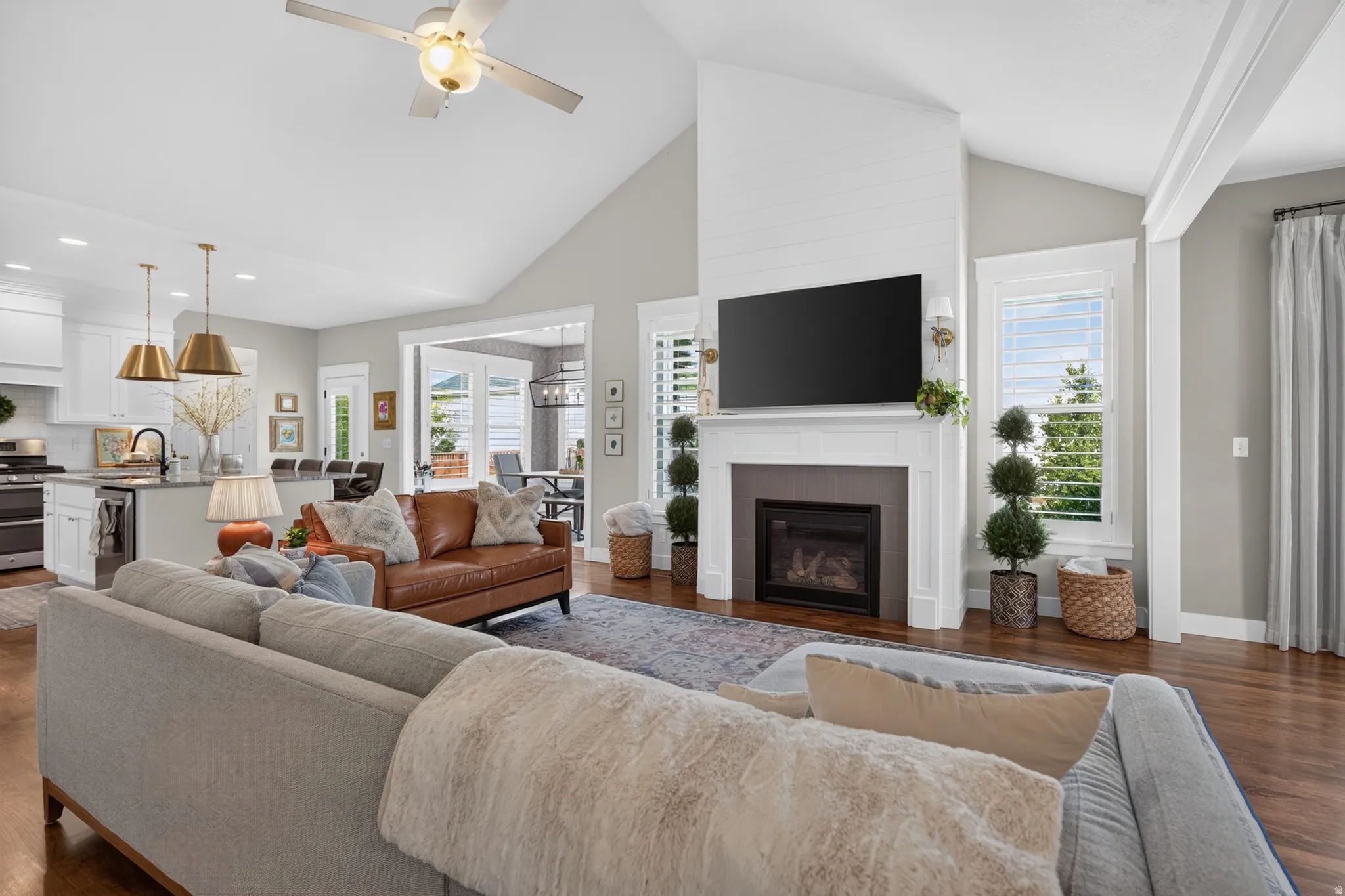 Vaulted ceiling with a ceiling fan, gas fireplace with mantel, recessed lighting, wood-finish flooring, and a kitchen island with pendant lighting