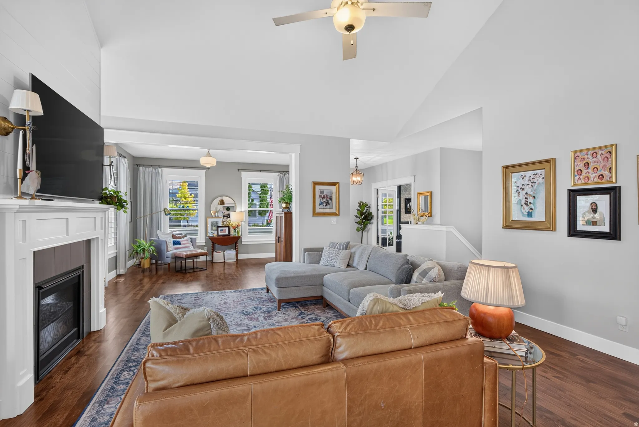 Vaulted ceiling with an integrated ceiling fan, wood-finish flooring, and a fireplace with a white mantel