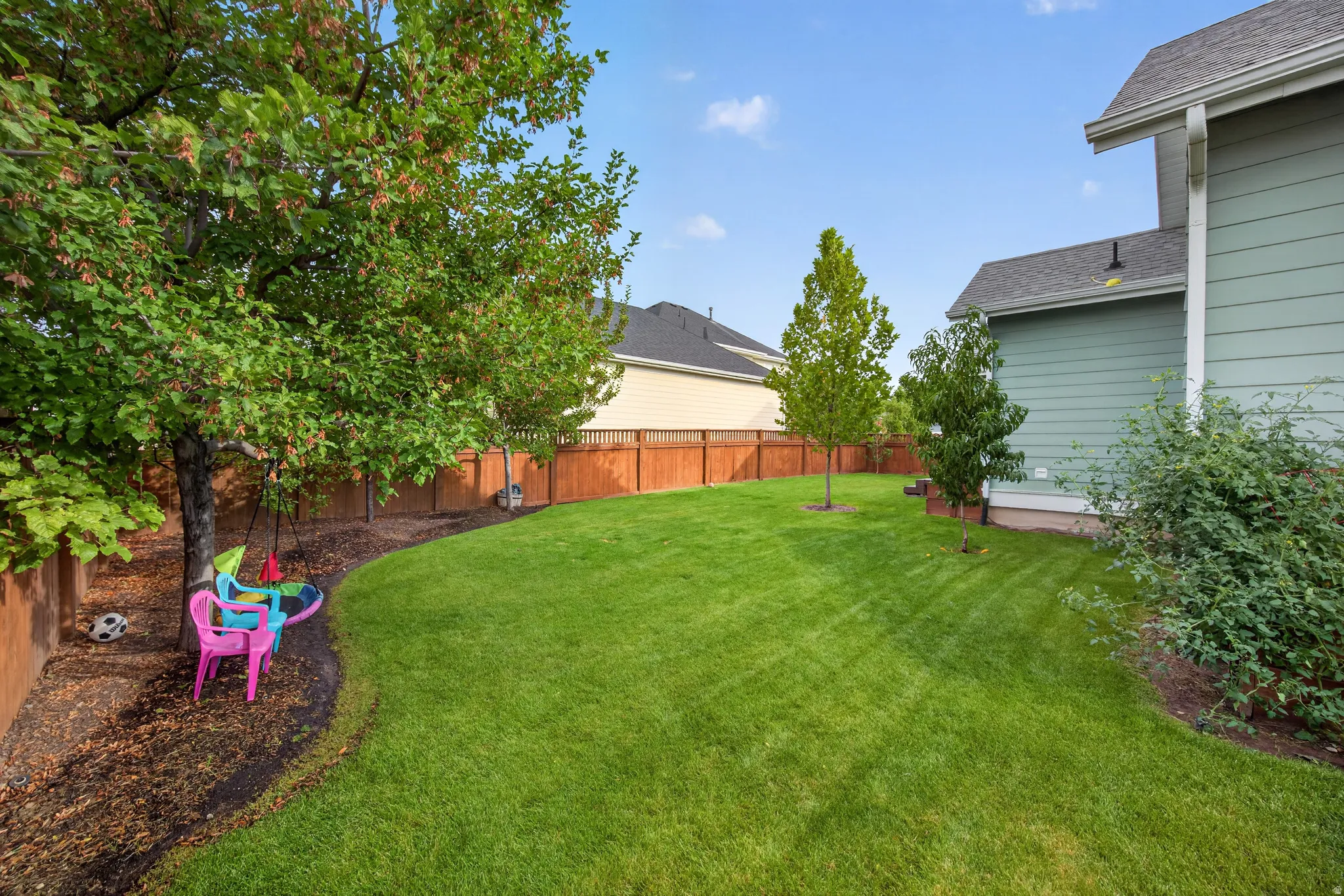 Expansive backyard featuring a manicured lawn, established trees, and a privacy fence
