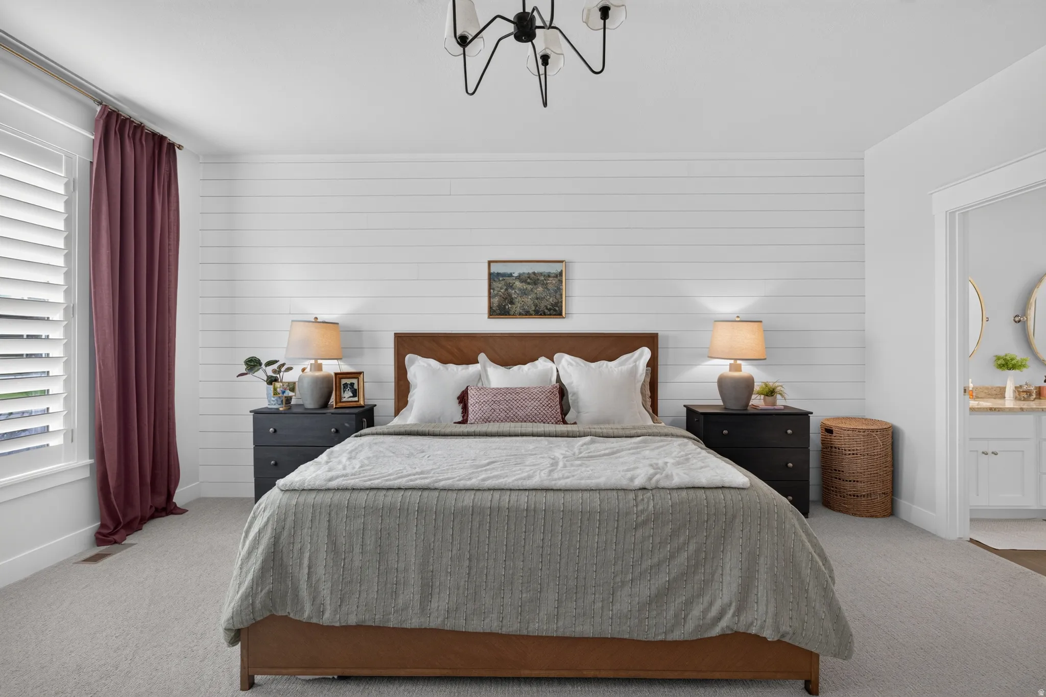 Carpeted room featuring a white shiplap accent wall, a modern chandelier, and plantation shutters