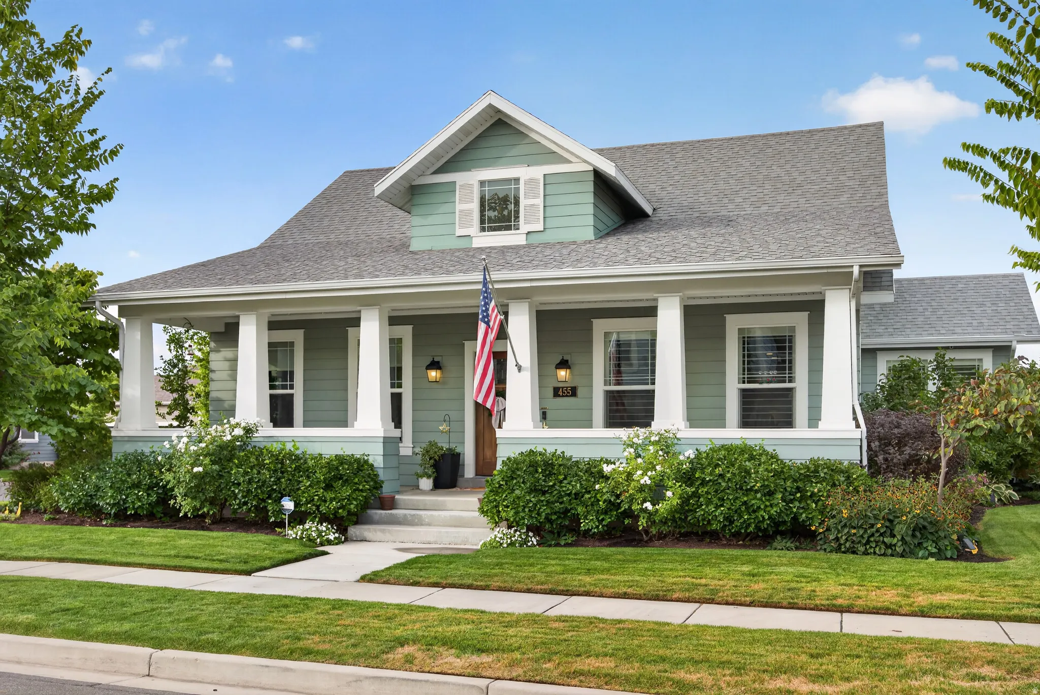 Craftsman-style residence featuring a covered front porch with substantial columns, light green siding, and a prominent dormer