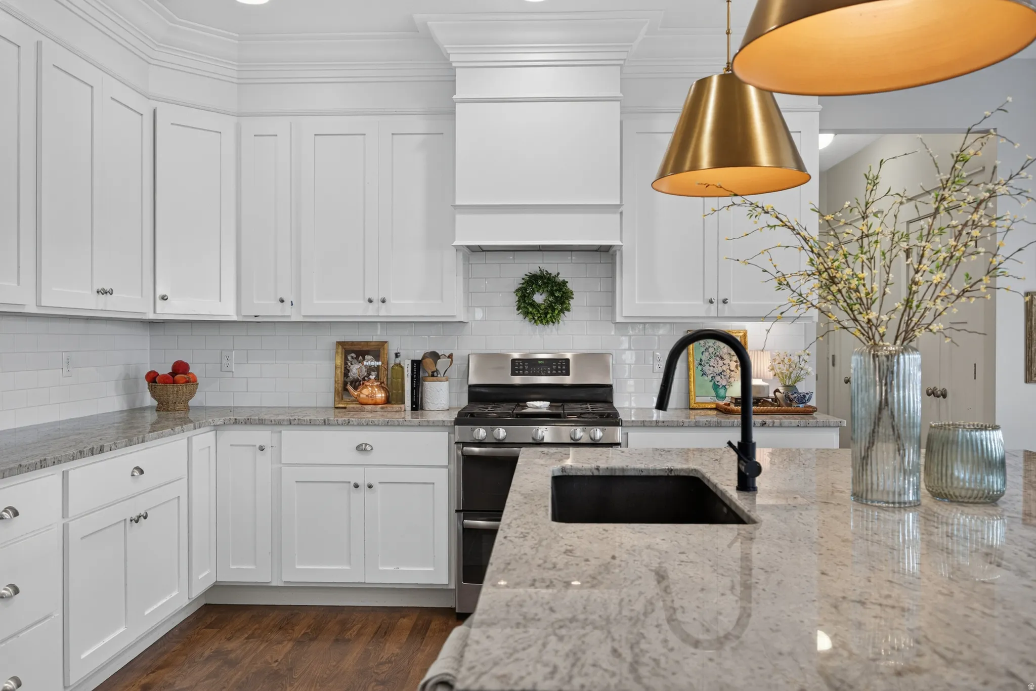 White shaker cabinetry, light-toned countertops, white subway tile backsplash, stainless steel range, and a black gooseneck faucet