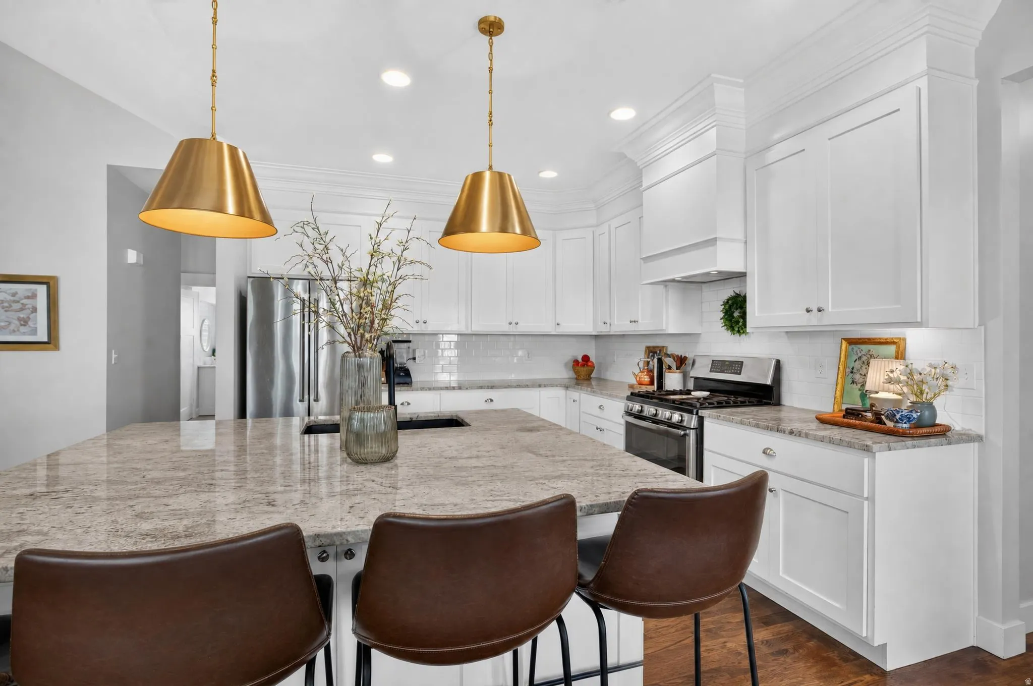 Kitchen featuring a large island with stone countertop, white shaker cabinetry, stainless steel appliances, and brass pendant lighting