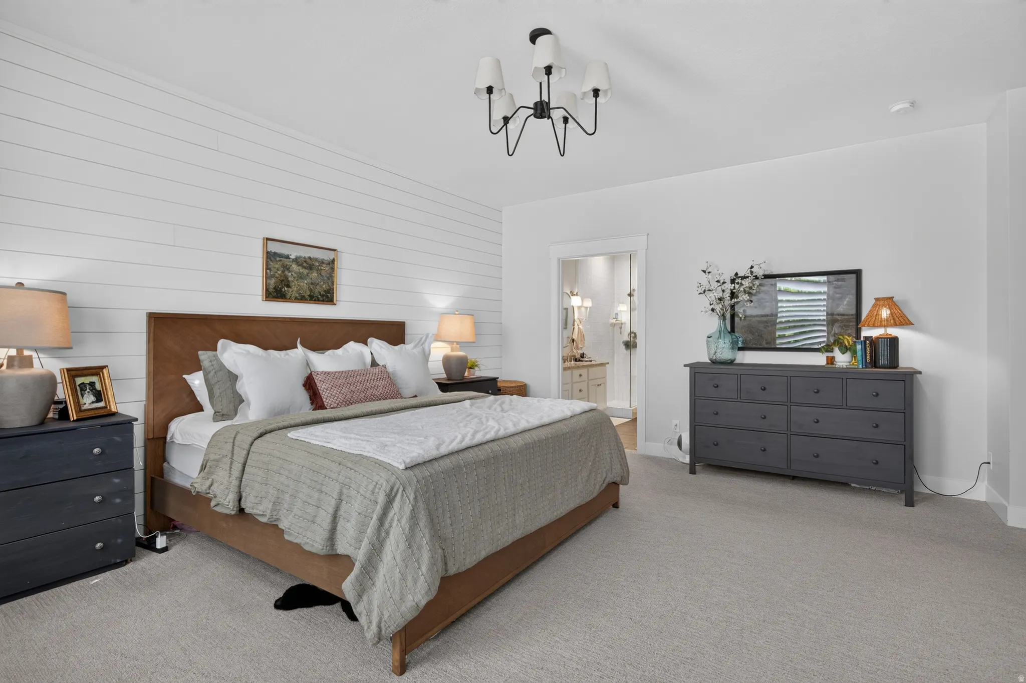 Wall-mounted lighting fixture, shiplap accent wall, light-toned carpeting, and a doorway to an adjoining bathroom
