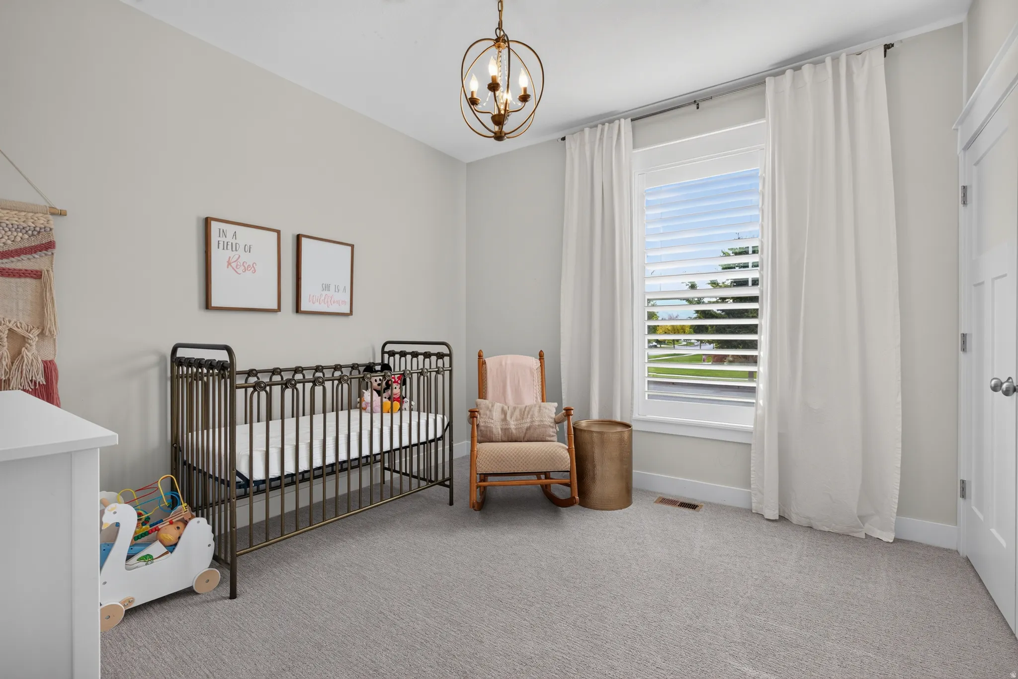 Spacious room featuring light gray walls, plush carpeting, a large window with white blinds, and a decorative ceiling fixture