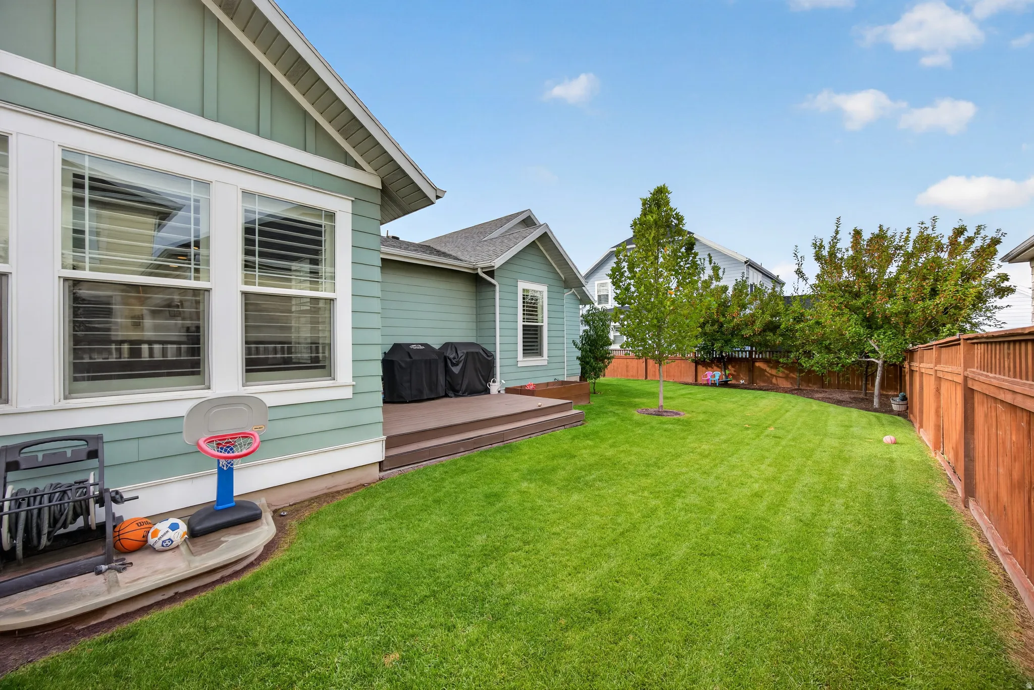 Expansive lawn area, multi-level composite deck, horizontal wood fencing, mature trees, and light green siding
