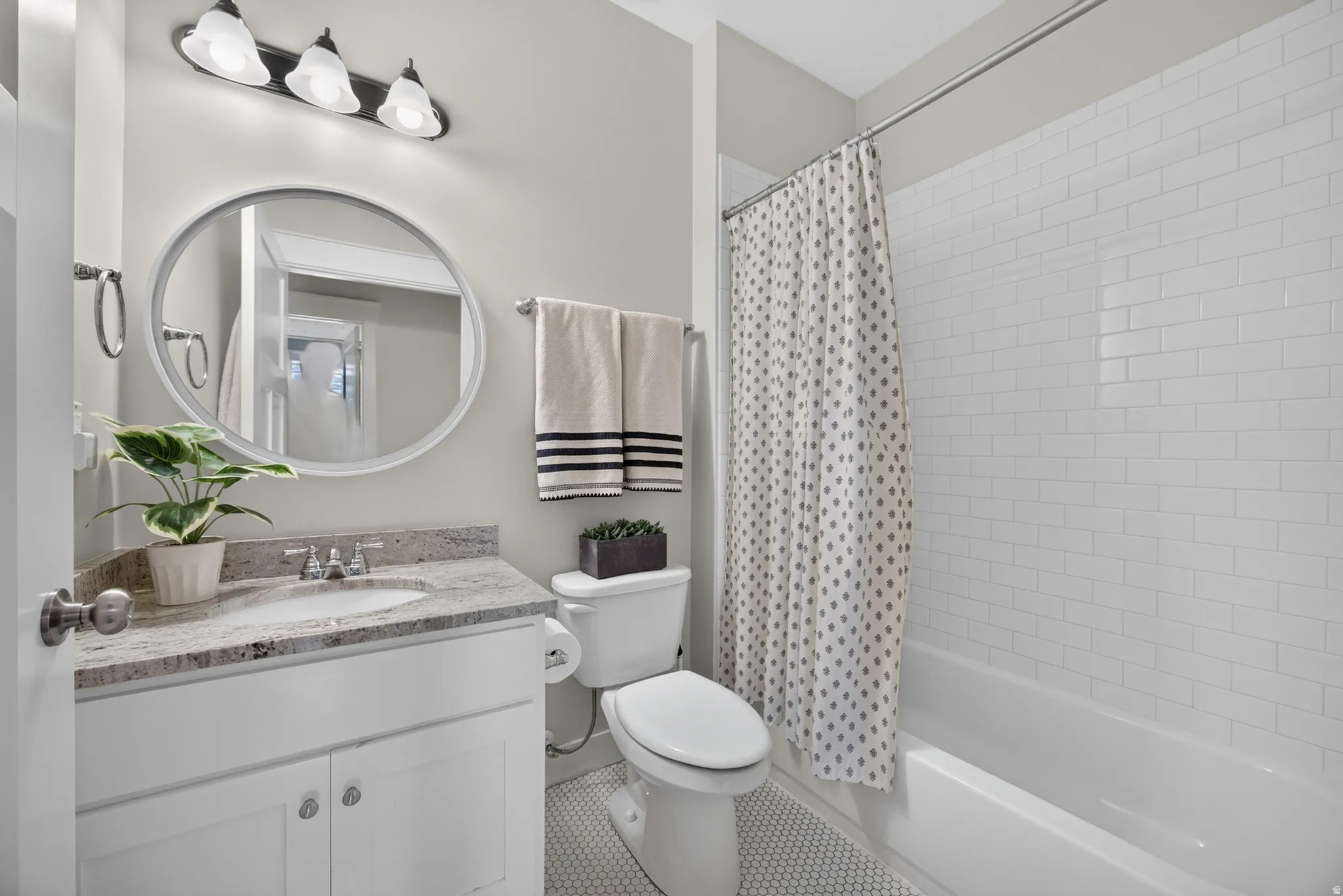 White subway tile bath surround, white vanity with stone countertop, round mirror, and tile flooring