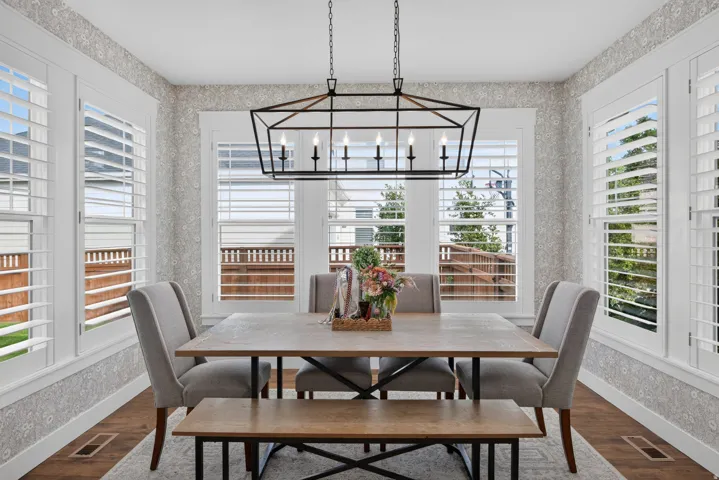 Hardwood-style flooring, white window shutters, patterned wall covering, and a contemporary linear chandelier