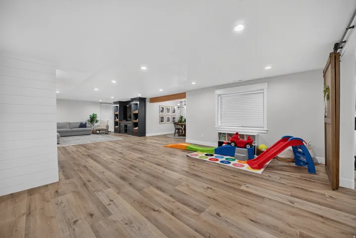 Expansive open-concept room featuring wood-finish flooring, recessed lighting, a built-in media center, a window with blinds, and shiplap wall accents