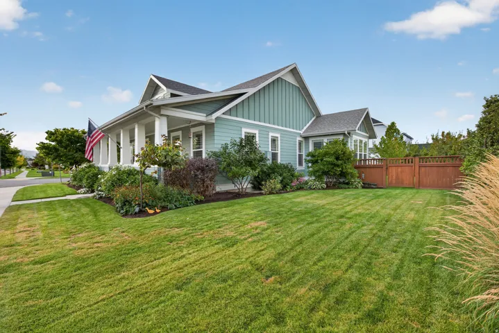 Exterior featuring board and batten siding, a covered porch with white columns, a gabled roofline, mature landscaping, and a wood privacy fence