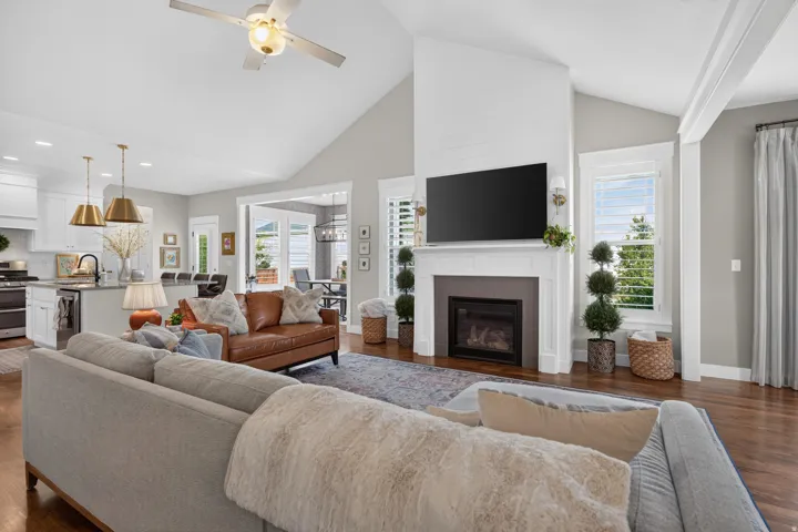 Vaulted ceiling with a ceiling fan, gas fireplace with mantel, recessed lighting, wood-finish flooring, and a kitchen island with pendant lighting