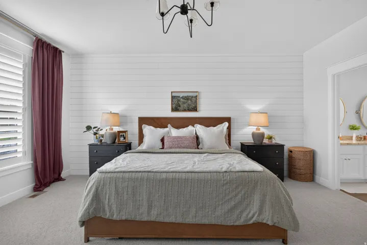 Carpeted room featuring a white shiplap accent wall, a modern chandelier, and plantation shutters