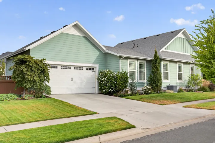 Light green siding with white trim, a two-car garage, concrete driveway, and mature landscaping