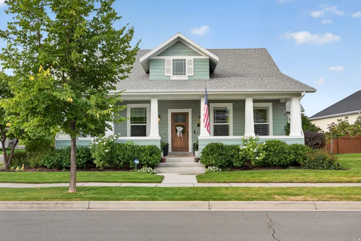 Craftsman-style home featuring a covered front porch with white columns, light green siding, and a prominent front-facing dormer
