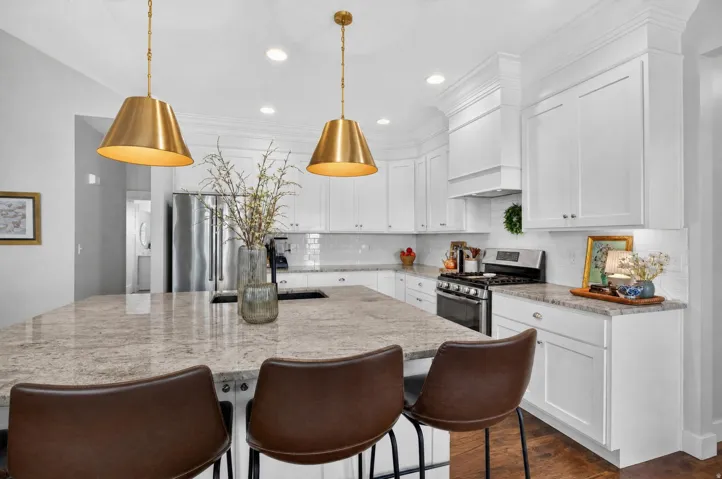 Kitchen featuring a large island with stone countertop, white shaker cabinetry, stainless steel appliances, and brass pendant lighting