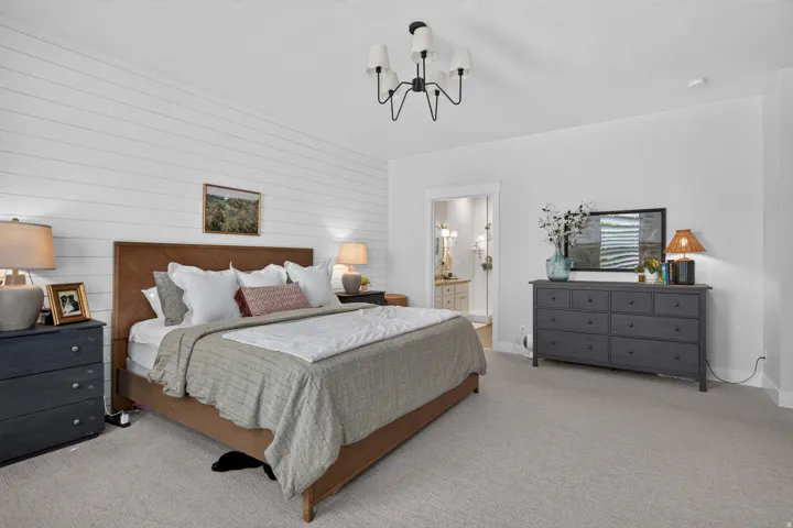 Wall-mounted lighting fixture, shiplap accent wall, light-toned carpeting, and a doorway to an adjoining bathroom