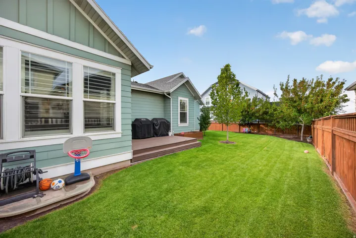 Expansive lawn area, multi-level composite deck, horizontal wood fencing, mature trees, and light green siding