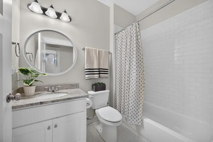 White subway tile bath surround, white vanity with stone countertop, round mirror, and tile flooring