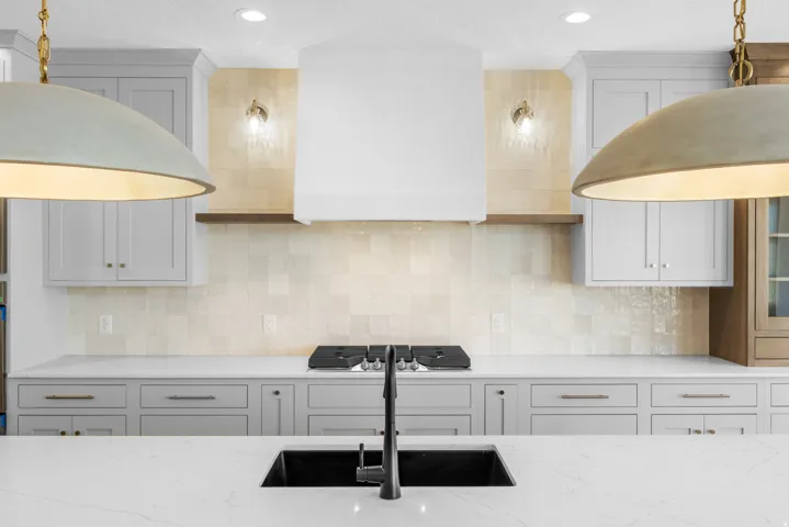 Contemporary kitchen featuring light gray cabinetry, a white range hood, a tiled backsplash, and a black sink with a matte black faucet