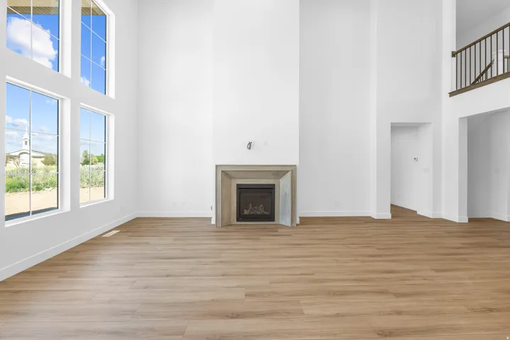 High ceilings with extensive window array, fireplace with stone-finish surround, wood-finish flooring, and upper-level railing with wood-finish top rail