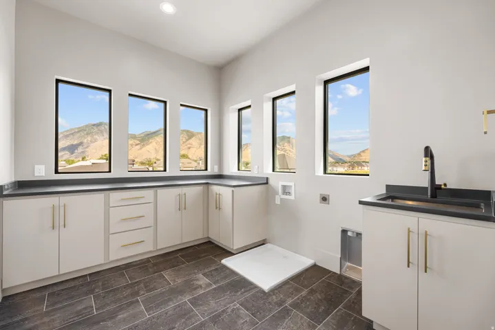 Built-in cabinetry with ample storage, dark countertops, a utility sink with a black faucet, large black-framed windows, and dark tile flooring