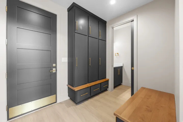 Mudroom featuring built-in cabinetry with gold-tone hardware, wood-finish flooring, a built-in bench, and a modern paneled door with a brass kick plate