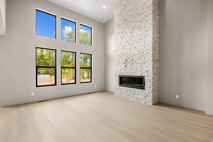 Vaulted ceilings, a full-height stone fireplace with an integrated linear firebox, extensive window placements, and light wood-finish flooring