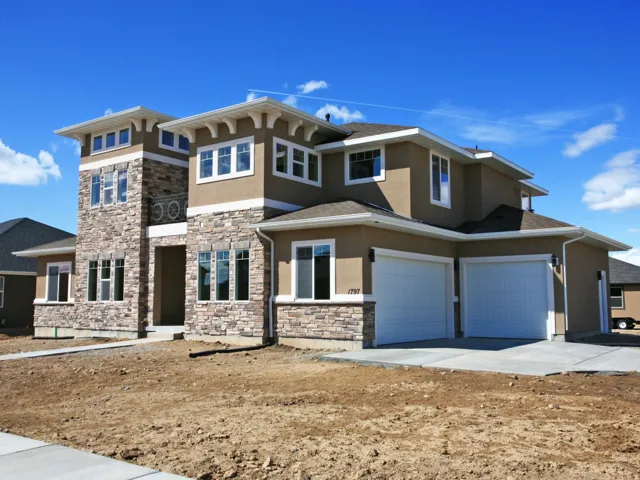 Stucco exterior featuring extensive stone accents, a multi-pane window configuration, and a two-car garage with panel doors