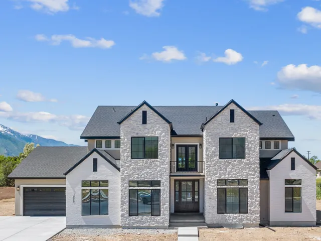 Modern architecture with a light-colored stone and stucco exterior, dark roof, dark-framed windows, and an attached two-car garage