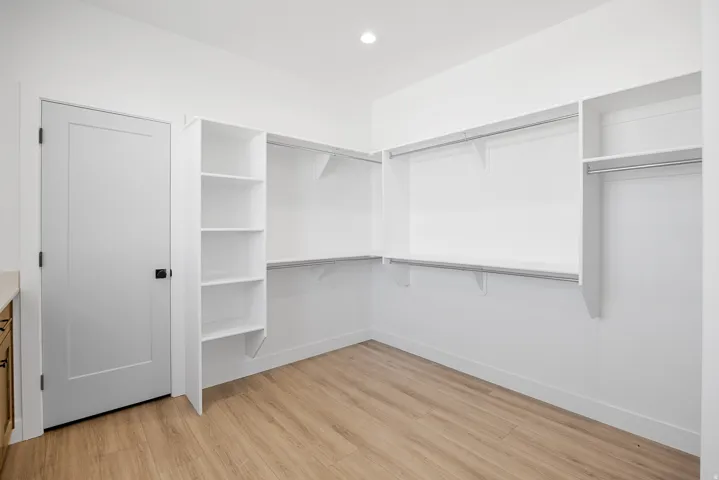 White interior door with dark hardware, built-in shelving, hanging rods, light wood-finish flooring, and recessed lighting