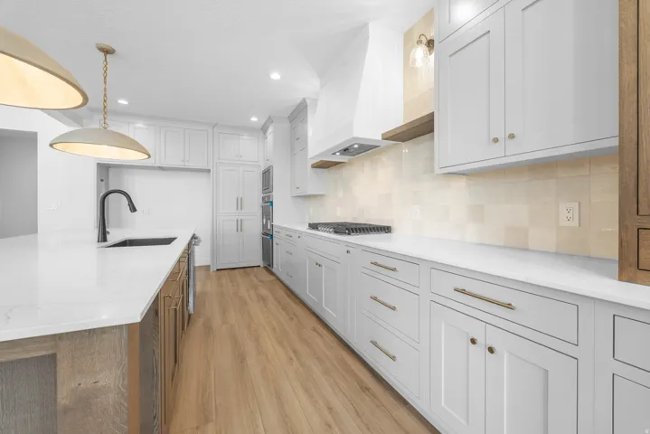 Kitchen featuring white cabinetry, light-toned wood-finish flooring, white countertops, built-in stainless steel appliances, and a tiled backsplash