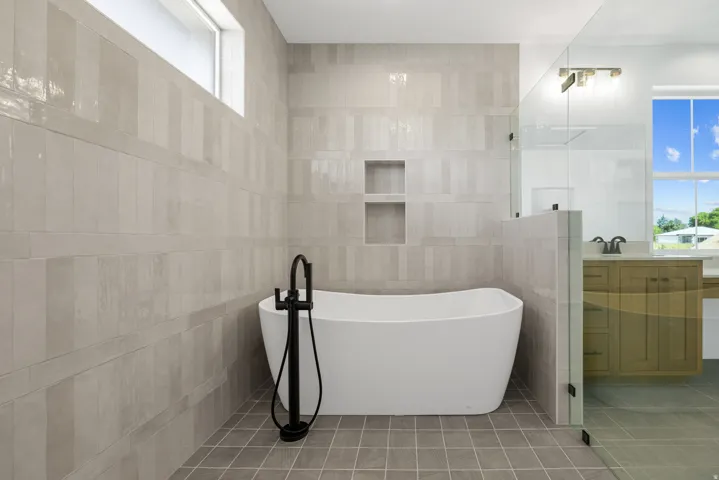 Freestanding soaking tub with a matte black floor-mounted faucet, tile walls, and a recessed tiled niche